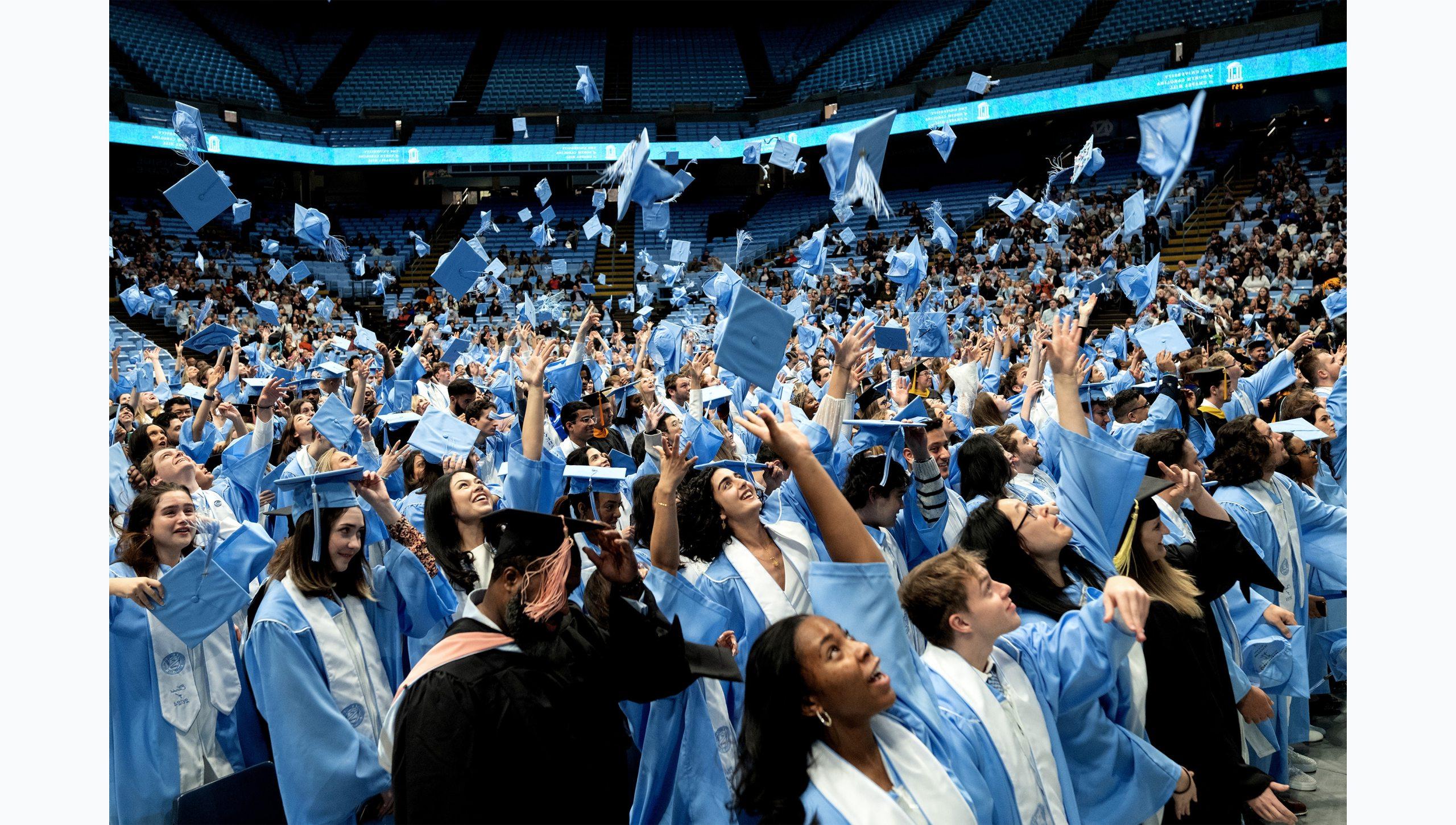 Graduates in Carolina Blue and black regalia throwing caps into the air in celebration at U.N.C. Chapel Hill's Winter Commencement.